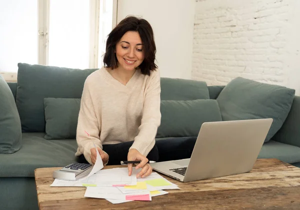 Joyeux jeune femme assise sur le canapé entouré de papiers calculer les dépenses et payer les factures — Photo