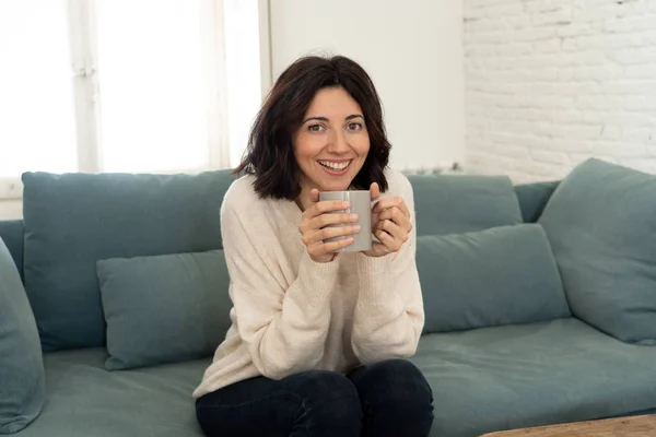 Lifestyle portrait of young pretty relaxed woman drinking hot coffee or chocolate feeling happy and cozy at home smiling happy on the couch. In leisure, peaceful life, happiness lifestyle concept.