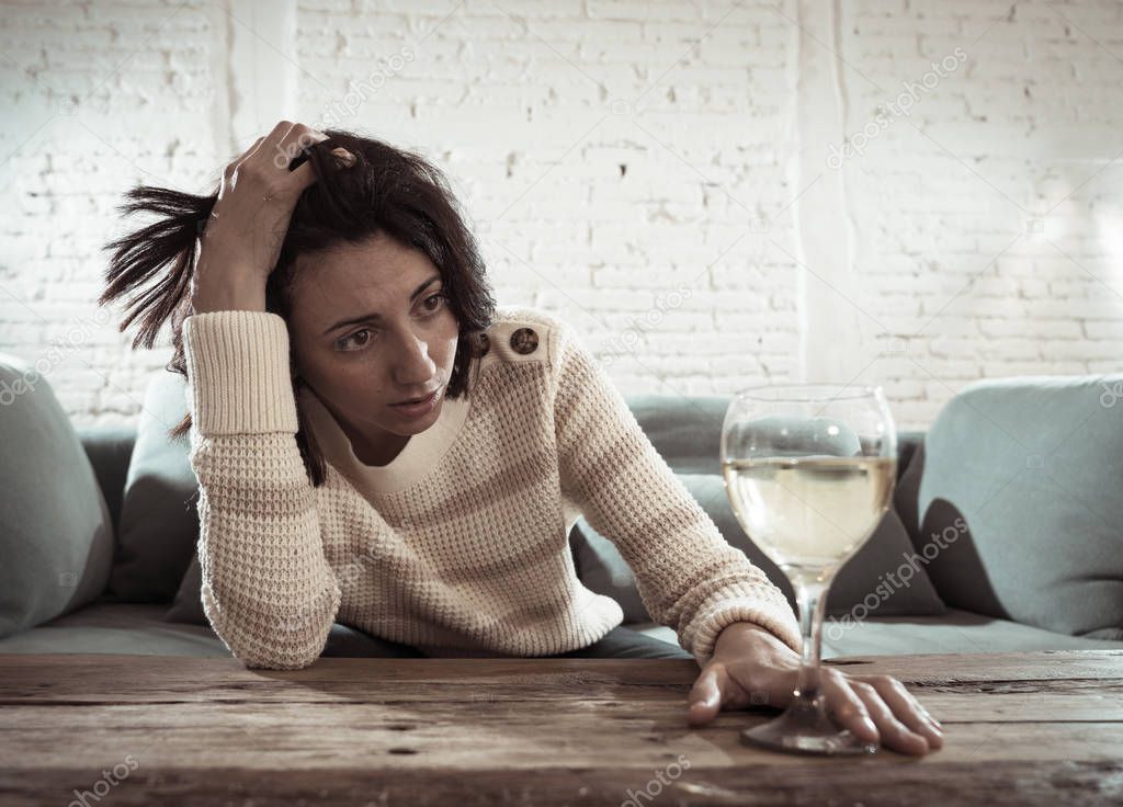 Stressed and hopeless young woman drinking a glass of wine alone at home. Feeling depressed, frustrated and weak, trying to feel better drinking. Unhealthy behavior, depression and alcoholism concept.