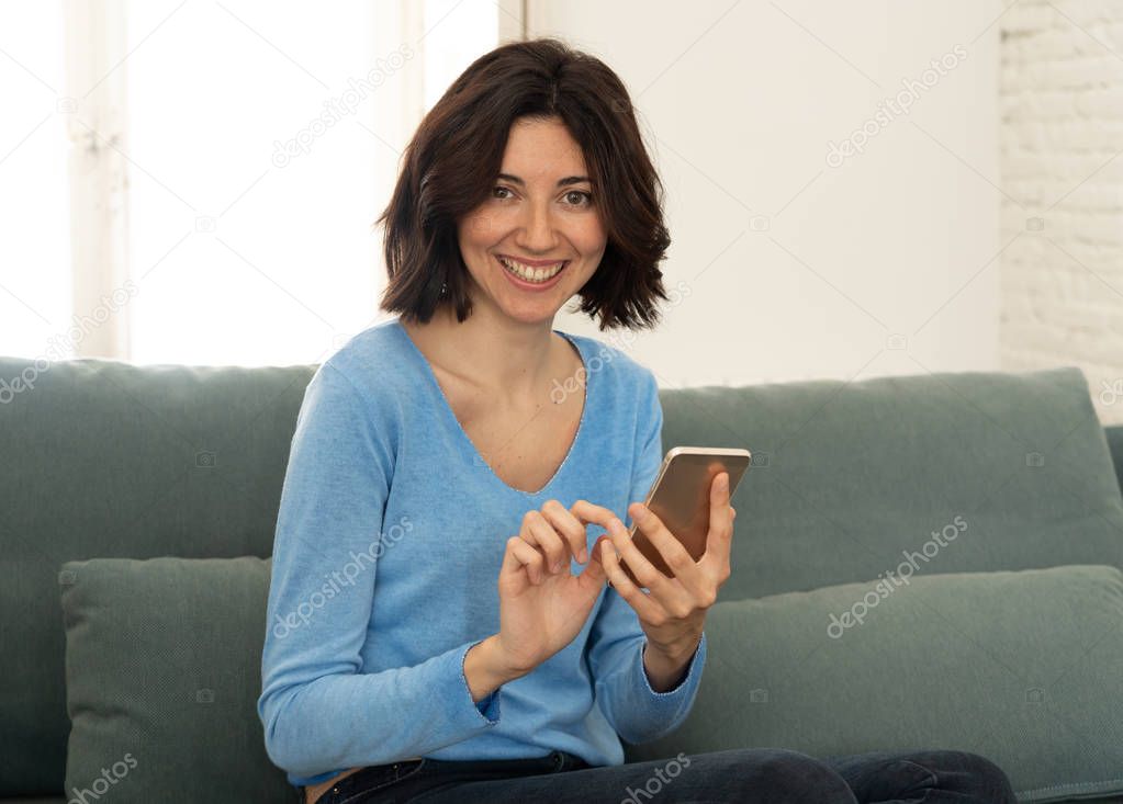 Happy young woman using her smart phone sitting on sofa at home. In leisure and mobile addiction