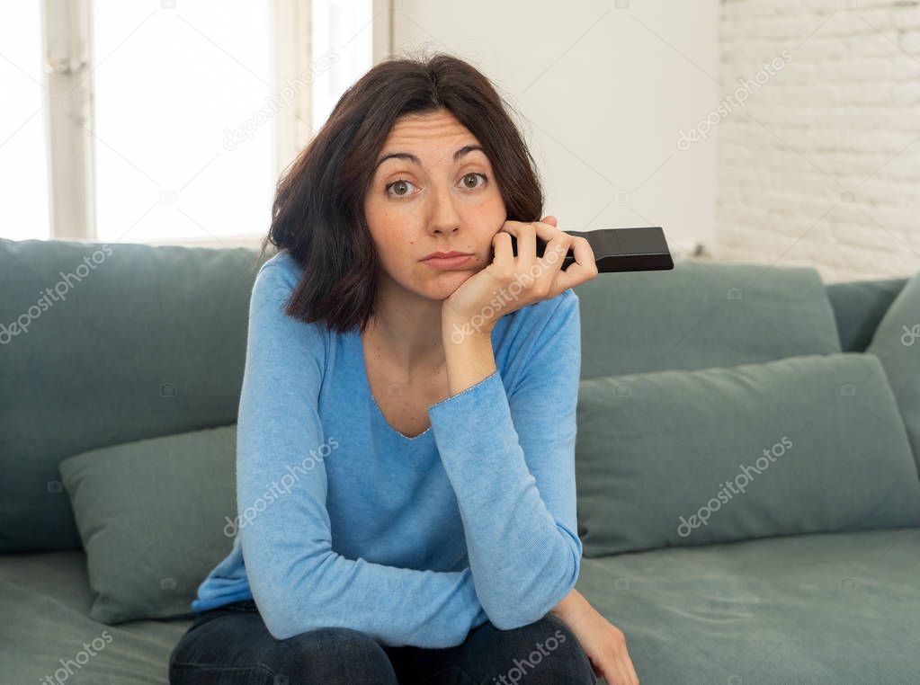 Young upset woman on sofa using control remote zapping bored of bad TV shows and programing . Looking disinterested, aloof and sleepless. People, too much bad television and Sedentary lifestyle.