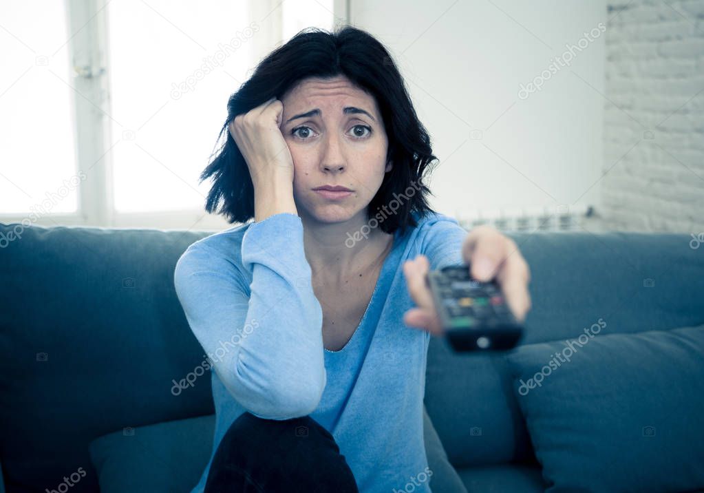 Young upset woman on sofa using control remote zapping bored of bad TV shows and programing . Looking disinterested, aloof and sleepless. People, too much bad television and Sedentary lifestyle.