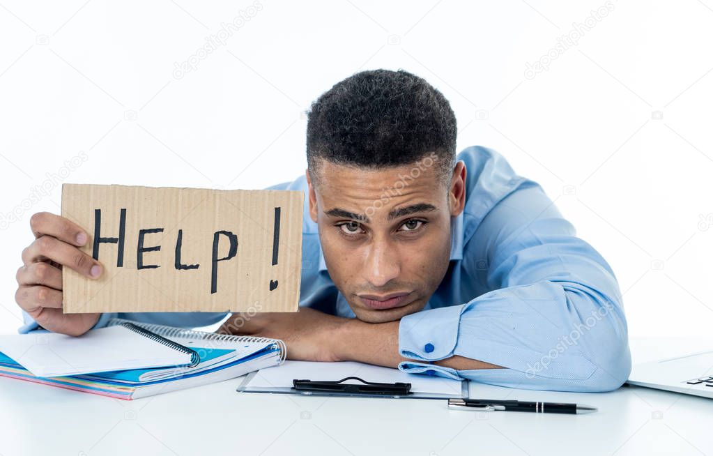 Desperate young attractive businessman working on computer laptop suffering stress at office going crazy holding a help sign. In stress at work, anxiety, technology problems and overwork concept.