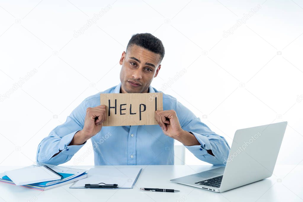 Desperate young attractive businessman working on computer laptop suffering stress at office going crazy holding a help sign. In stress at work, anxiety, technology problems and overwork concept.