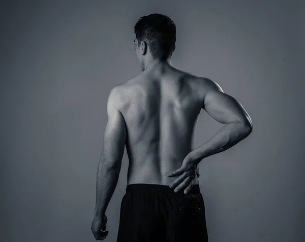 年轻的肌肉健身男子触摸和抓住他的下背部遭受强烈的疼痛后锻炼 在中性背景上隔离 在运动损伤不正确的姿势问题和身体保健 — 图库照片