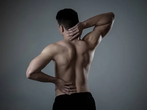 Young muscular fitness man touching and grabbing his neck and lower back suffering cervical pain isolated on neutral background. In sport and workout injury, Incorrect posture problems and body care.