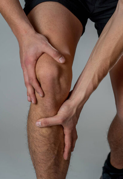 Young fit man holding knee with hands in pain after suffering muscle injury broken bone leg pain sprain or cramp during running workout. In Body pain and sport training injury and body health care.