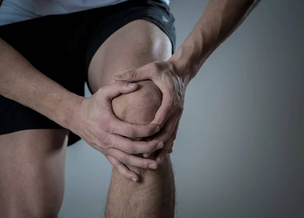 年轻的适合男子抱着膝盖与手在痛苦后遭受肌肉损伤断骨腿疼痛扭伤或抽筋在跑步锻炼 在身体疼痛和运动训练损伤和身体保健 — 图库照片