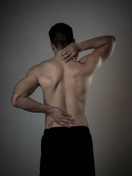 Young muscular fitness man touching and grabbing his neck and lower back suffering cervical pain isolated on neutral background. In sport and workout injury, Incorrect posture problems and body care. — Stock Image Young Muscular Fitness Man Touching Grabbing His Neck Lower Back Stock Image