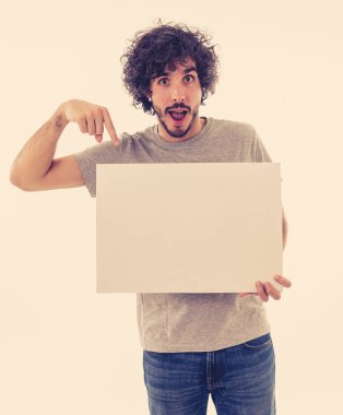 Komik ve iyi görünümlü milenyal adam gösteren ve metin için kopya alanı ile boş tahta işaret. Samimi ve heyecanlı genç şık adam reklam için boş poster tutuyor. Pazarlama konsepti.