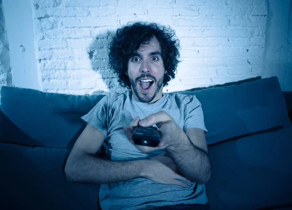 Lifestyle portrait of tv show fan man watching excited favorite series movie or soccer football game in online TV late at night. In people streaming content addiction and entertainment concept.