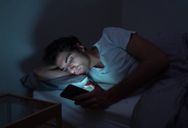 Addicted Man sohbet ve yatakta gece geç saatlere kadar akıllı telefon ile Internette sörf. Sıkılmış, uykusuz ve kasvetli ışık ile karanlık odada yorgun. Uykusuzluk ve mobil bağımlılık kavramı.