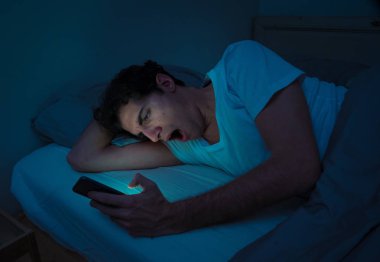 Addicted Man sohbet ve yatakta gece geç saatlere kadar akıllı telefon ile Internette sörf. Sıkılmış, uykusuz ve kasvetli ışık ile karanlık odada yorgun. Uykusuzluk ve mobil bağımlılık kavramı.