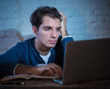 Aşırı çalıştı ve yorgun erkek öğrenci uyku, endişeli ve üzücü yorgunluk hissi düşmek için çalışmıyor laptop gece geç saatlere kadar çalışıyor. Moody koyu ışık. Final sınavları online öğrenme ve aşırı çalışma kavramı.