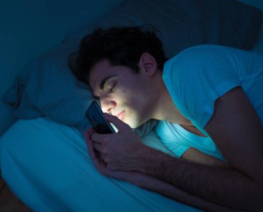Sosyal medya genç adam yatakta gece akıllı cep telefonu ile uykuya düşmek Addicted. mobil ekran ışık ile karanlık yatak odasında uyku adam yaşam tarzı portre. Mobil kullanım bağımlılığı.