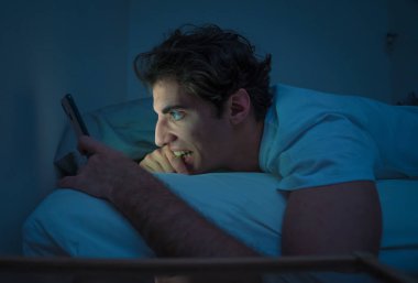 Sosyal medya genç adam sohbet ve yatakta gece akıllı telefon Internette sörf Addicted. Mobil ekran ışığı ile karanlık yatak odasında uykusuz. Uykusuzluk ve çevrimiçi ağ bağımlılığı.