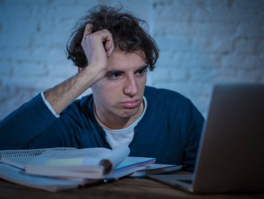 Aşırı çalıştı ve yorgun erkek öğrenci uyku, endişeli ve üzücü yorgunluk hissi düşmek için çalışmıyor laptop gece geç saatlere kadar çalışıyor. Moody koyu ışık. Final sınavları online öğrenme ve aşırı çalışma kavramı.