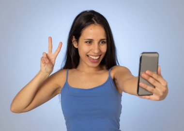Cep telefonu ile selfie çeken genç serin güzel latin genç kadın Stüdyo çekim eğlenceli ve mobil ve sosyal medya bağımlılığı kullanarak bin yıllık nesil güzel seksi görünümlü.