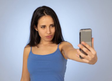 Cep telefonu ile selfie çeken genç serin güzel latin genç kadın Stüdyo çekim eğlenceli ve mobil ve sosyal medya bağımlılığı kullanarak bin yıllık nesil güzel seksi görünümlü.