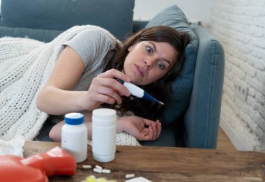Sağlık ve tıp. Evde kanepede yatan hasta kadın baş ağrısı burun ağrısı ile hasta burun termometre hissi ile yüksek sıcaklık kontrol yorgunluk ve huzursuz işe gitmek mümkün değil.