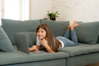 Güzel sevimli sevimli kız öğrenci oynarken ve dizüstü bilgisayar da internette sörf gülümseyerek ve evde kanepede yatarken. Dijital teknoloji, internet kullanımı ve yaşam tarzı konsepti.
