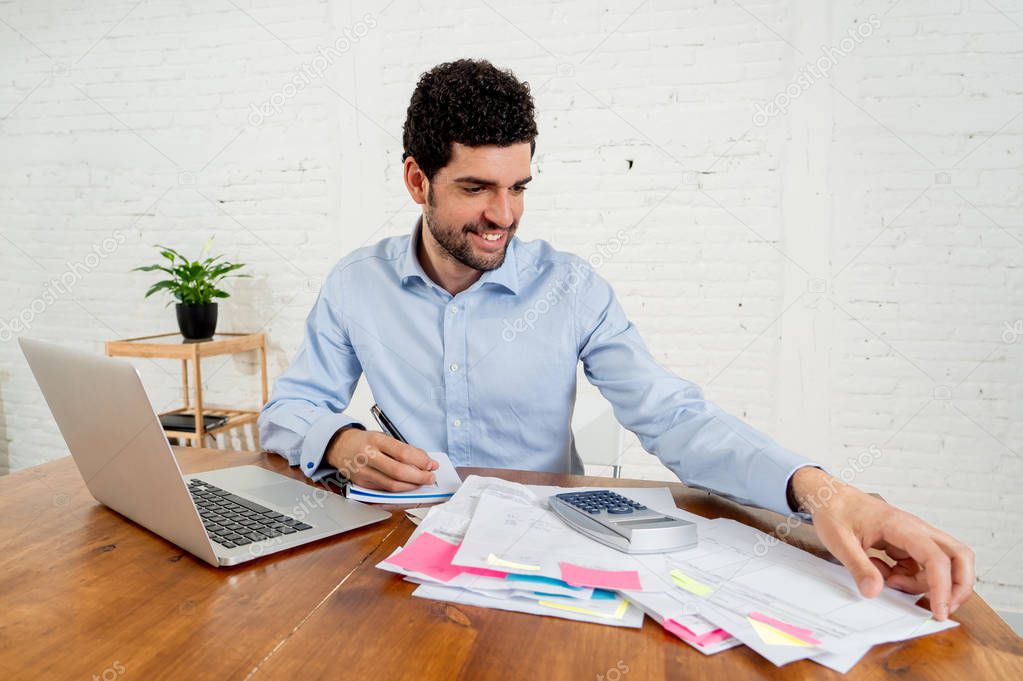 Happy attractive entrepreneur man calculating costs, charges, mortgage, taxes or paying bills with documents and laptop at home office. In online banking and Success business finances free of debts.