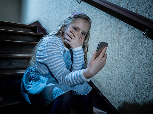 Sad depressed girl Bullied by text message humiliated online social media by classmates. Sad depressed young girl victim of cyberbullying by mobile phone sitting on stairs feeling lonely hopeless.