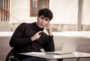 Genç adam sohbet ve mesajlaşma konuşmak için akıllı cep telefonu uygulaması kullanarak ve bir kentsel Avrupa şehir kahve terasında selfie alarak. Online dating mobil uygulama Internet bağlantıları ve teknoloji kullanımı.