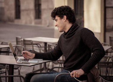 Yakışıklı genç adam bir Avrupa şehir kahve dükkanında teras dışında dizüstü bilgisayar üzerinde çalışıyor. Öğrenci Duygu mutlu ve memnun. Avrupa'da online eğitim ve teknoloji konsepti nde seyahat.