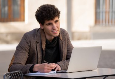 Yakışıklı genç adam bir Avrupa şehir kahve dükkanında teras dışında dizüstü bilgisayar üzerinde çalışıyor. Öğrenci Duygu mutlu ve memnun. Avrupa'da online eğitim ve teknoloji konsepti nde seyahat.