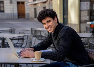 Yakışıklı genç adam bir Avrupa şehir kahve dükkanında teras dışında dizüstü bilgisayar üzerinde çalışıyor. Öğrenci Duygu mutlu ve memnun. Avrupa'da online eğitim ve teknoloji konsepti nde seyahat.