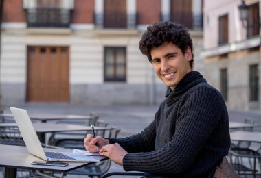 Yakışıklı genç adam bir Avrupa şehir kahve dükkanında teras dışında dizüstü bilgisayar üzerinde çalışıyor. Öğrenci Duygu mutlu ve memnun. Avrupa'da online eğitim ve teknoloji konsepti nde seyahat.