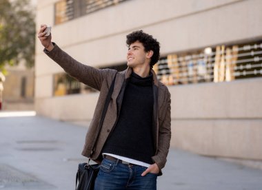 Heyecanlı Trendy genç adam selfie veya Avrupa şehir Caddesi veya üniversite kampüsünde tatil akıllı cep telefonu bloglama alarak. Tatil ve teknoloji bağlantı ve sosyal medya konsepti.
