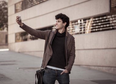 Heyecanlı Trendy genç adam selfie veya Avrupa şehir Caddesi veya üniversite kampüsünde tatil akıllı cep telefonu bloglama alarak. Tatil ve teknoloji bağlantı ve sosyal medya konsepti.