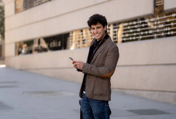 Fashion college man in his twenties happy checking blog or chatting on the internet with friend on smart mobile phone app in european city outdoors city. In communication technology and travel Europe.