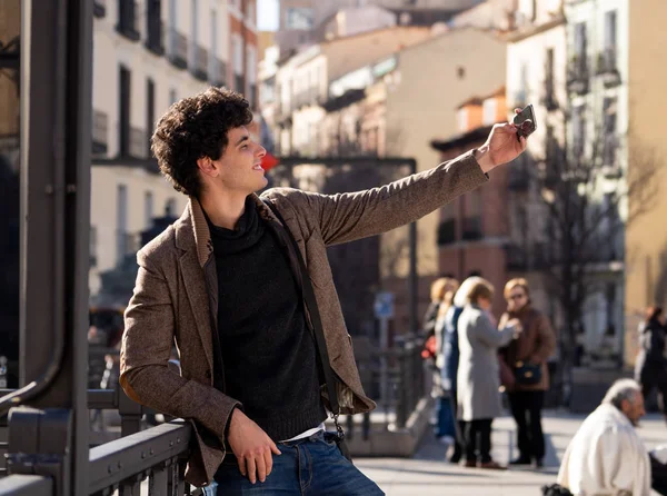 Heyecanlı Trendy genç adam selfie veya Avrupa şehir Caddesi veya üniversite kampüsünde tatil akıllı cep telefonu bloglama alarak. Tatil ve teknoloji bağlantı ve sosyal medya konsepti.