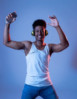 Güçlü afro-Amerikan genç dansçı adam müzik online dans dinleme ve kulaklıkile şarkı. İnternet Müzik ve teknoloji konseptinde disko dans pisti neon ışıklı sanatsal portre.