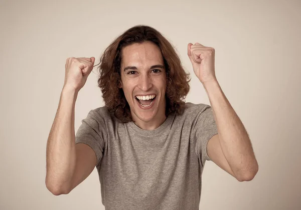 Portrait of very excited young man celebrating winning the lottery or having great success. Teenager with long hair and surprised and happy gestures. In People facial Expression and Human Emotions.