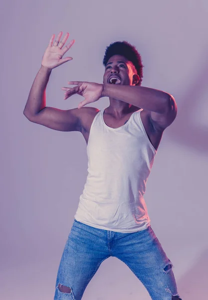 Portrait of inspired cool african american teenager man dancing feeling the music and enjoying life on blue moody disco neon light background. In People, Youth Party night lifestyle. Studio shot.