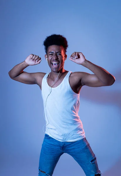 Strong african american young dancer man listening to music online dancing and singing with earphones. Artistic portrait with disco dance floor neon light in Internet Music and technology concept.