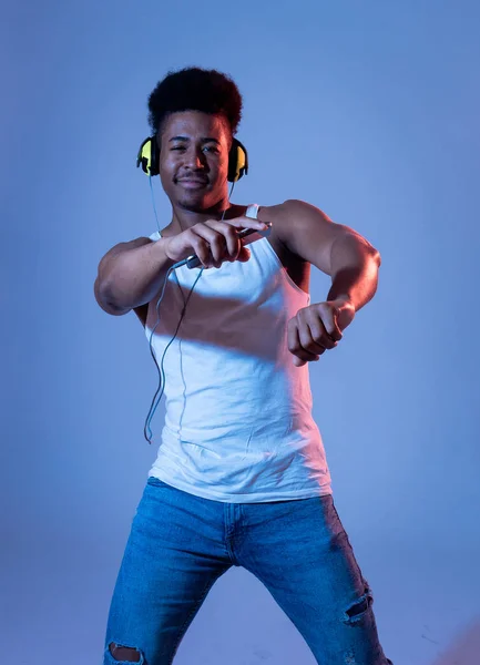 強いアフリカ系アメリカ人の若いダンサーの男性は 音楽のオンラインダンスを聴き ヘッドフォンで歌います インターネットミュージックとテクノロジーコンセプトのディスコダンスフロアネオンライトを持つ芸術的な肖像画 — ストック写真