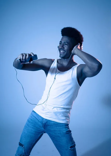 Strong african american young dancer man listening to music online dancing and singing with headphones. Artistic portrait with disco dance floor neon light in Internet Music and technology concept.