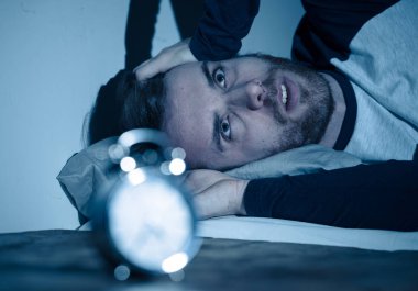 Uykusuz ve çaresiz genç beyaz adam Uykusuz geceleri uyku mümkün değil, hayal kırıklığına ve endişe saat uykusuzluk stres ve uyku bozukluğu kavramı muzdarip bakıyor.