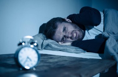 Uykusuz ve çaresiz genç beyaz adam Uykusuz geceleri uyku mümkün değil, hayal kırıklığına ve endişe saat uykusuzluk stres ve uyku bozukluğu kavramı muzdarip bakıyor.