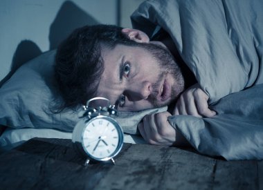 Ruh sağlığı, uykusuzluk ve uyku bozuklukları. Sinirli ve umutsuz uykusuz adam alarm saat uyanık gece uyanma anksiyete İşteki stres neden acı uyku mümkün değil bakıyor.