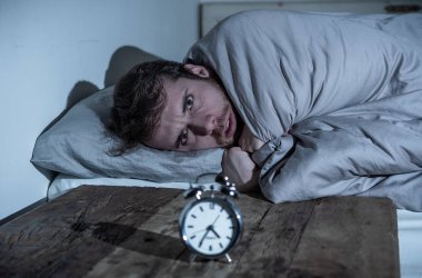 Ruh sağlığı, uykusuzluk ve uyku bozuklukları. Sinirli ve umutsuz uykusuz adam alarm saat uyanık gece uyanma anksiyete İşteki stres neden acı uyku mümkün değil bakıyor.