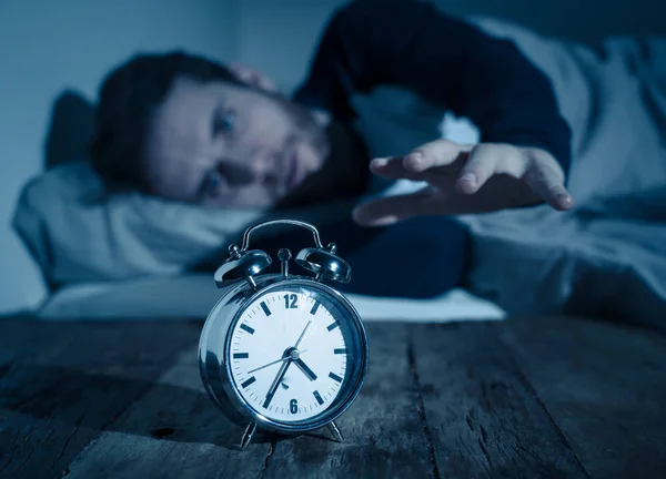 Insomnia Stress and Sleeping disorder concept. Sleepless desperate young caucasian man awake at night not able to sleep, feeling frustrated and worried looking stressed and concerned at alarm clock.