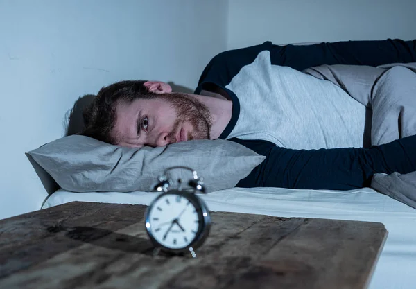 Mental health, Insomnia and sleeping disorders. Frustrated and hopeless sleepless man looking in distress at alarm clock awake at night not able to sleep suffering anxiety caused by stress at work.