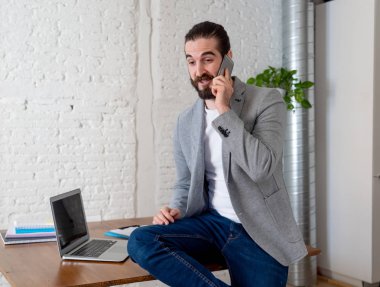 Modern stüdyo ofisinde dizüstü çalışırken hipster başarılı iş sahibi mobil akıllı telefon üzerinde iş konuşurken Portresi. İnsanlar başlangıç küçük İş İletişimi ve teknoloji olarak.