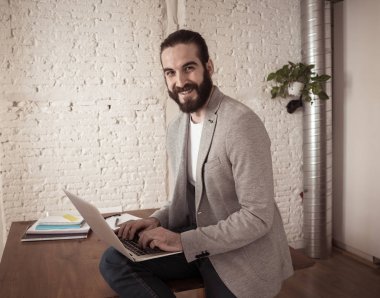 Başarılı hipster girişimci onun modern stüdyo ev ofisinde dizüstü bilgisayar üzerinde çalışıyor. Kendi iş başarısı ile mutlu ve kendinden emin görünümlü. In People başlangıç ve başarılı genç işadamları kavramı.
